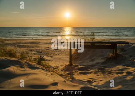 Leere Holzbank und schöner goldener Sonnenuntergang am Strand. Sonnenuntergang im Meer an ruhigen Abend. Niemand Stockfoto