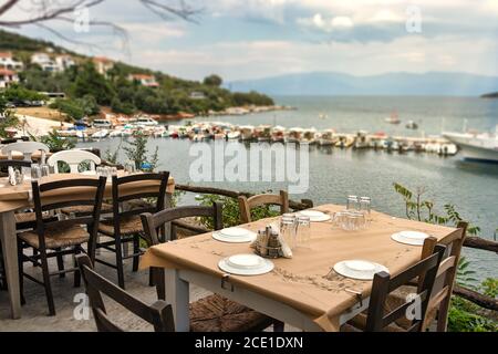 Traditionelle Holztische und Stühle einer griechischen Taverne mit Blick auf den Hafen von Amaliapoli, Griechenland Stockfoto