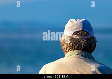 Nahaufnahme des Rückens eines älteren Mannes Kopf mit grauen Haaren trägt eine Tasse Blick auf das Meer Stockfoto