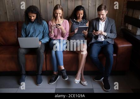 Diverse Jugendliche verwenden elektronische Geräte, sitzen in der Zeile Stockfoto