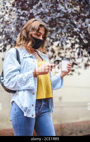 Vertikales Porträt einer jungen rothaarigen Frau mit Marke Telefon und halten eine Tasse Kaffee zum Mitnehmen in Die Straße Stockfoto