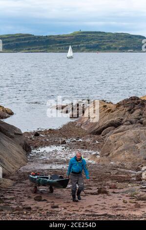 Portencross, Schottland, Großbritannien. August 2020. UK Wetter: Ein Fischer zieht sein Boot am Ufer mit der Isle of Little Cumbrae im Hintergrund hoch. Kredit: Skully/Alamy Live Nachrichten Stockfoto