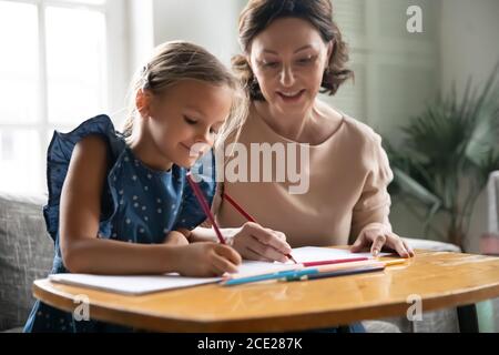 Liebevoll fürsorgliche ältere Frau hilft kleinen Enkelin mit Schulaufgaben. Stockfoto