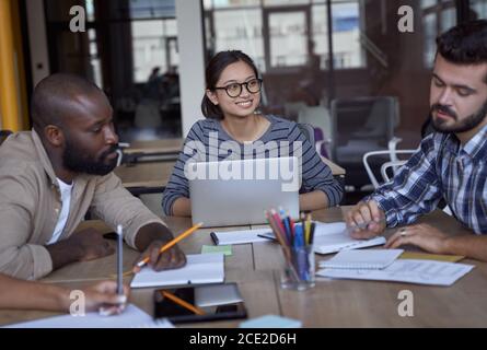 Zu einem Meeting. Drei junge multikulturelle Geschäftsleute arbeiten im modernen Büro zusammen, diskutieren Projekte oder teilen Ideen Stockfoto