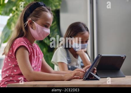 Verschiedene ethnische Zugehörigkeit schöne Mädchen im Schulalter sitzen am Schreibtisch mit tragbaren Computer. Mit modernen Gerät ignorieren einander, das Studium entfernt durch Draht Stockfoto