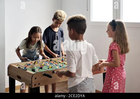 Gruppe von multikulturellen niedlichen Kinder stehen drinnen verbringen Spielzeit mit Freunden spielen Tischfußball zusammen. Tischversion von Fußballfans. Mit Fu Stockfoto