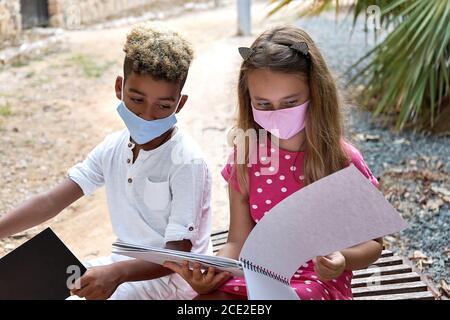 Zwei multiethnische liebenswert 9s 10s Jahre Mädchen und Junge sitzen auf Bank reden ihre Zeichnungen diskutieren verbringen Freizeit zusammen im Freien. Freizeit, Hobby und p Stockfoto