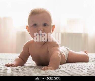 Ein vier Monate altes Baby liegt auf dem Bauch und schaut nach oben. Das Baby lächelt. Gute Laune Stockfoto