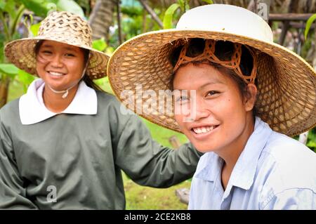 Zwei junge Thai-Frauen mit einladendem Lächeln tragen ihre einzigartigen Thai-Strohhüte auf dem Ayothaya Floating Market in Ayutthaya, Thailand Stockfoto