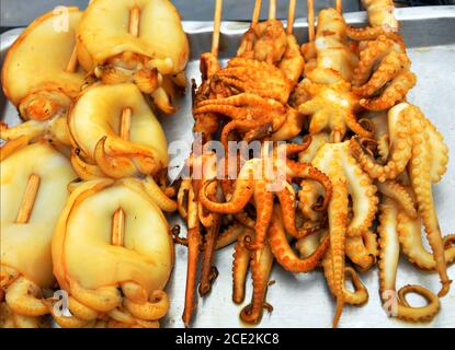 Nahaufnahme von Golden Calamari und Oktopus auf Holzspießen, die von Straßenverkäufern in Bangkok, Thailand, angeboten werden Stockfoto