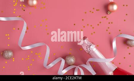Champagner-Flasche mit Konfetti-Sternen und Party-Streamer auf rosa Hintergrund. Weihnachts- oder Geburtstagsfeier Konzept. Flach liegend, Draufsicht Stockfoto