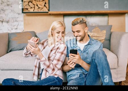 Lächelndes junges Paar, das sich zu Hause auf der Couch mit dem Smartphone entspannt Stockfoto