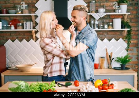 Schöne junge Paar gegenseitig füttern und lächelnd beim Kochen in der Küche zu Hause Stockfoto