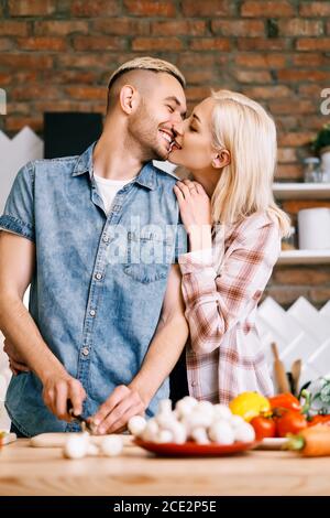Junges Paar küssen und Kochen zusammen vegetarische Mahlzeit in der Küche zu Hause Stockfoto