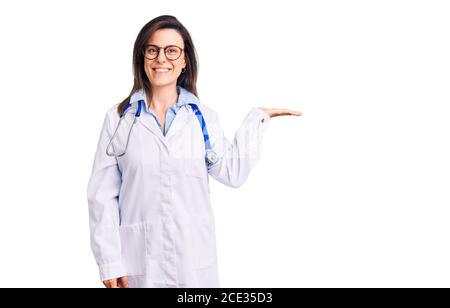 Junge schöne Frau trägt Arzt Stethoskop und Brille lächelnd fröhlich präsentiert und zeigt mit Handfläche Blick auf die Kamera. Stockfoto