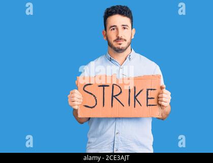 Junge hispanic Mann hält Streik Banner Karton Denken Haltung und Nüchterner Ausdruck, der selbstbewusst aussieht Stockfoto