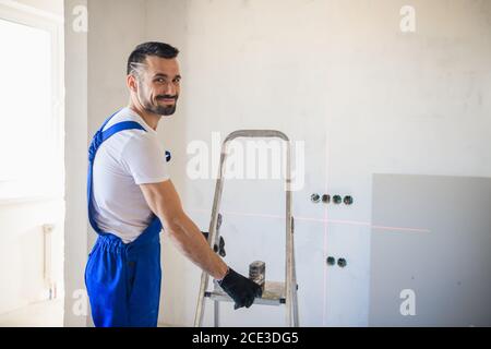 Ein bärtiger Mann bewegt eine Aluminiumtreppe um die Zimmer Stockfoto