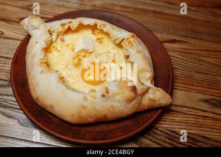 Draufsicht auf traditionelle adjarianische Khachapuri - Open gebackene Kuchen mit geschmolzenem Salzkäse Suluguni und Eigelb auf Holztablett. Traditionelle georgische Küche Stockfoto