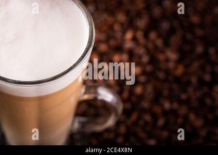 Kaffee Latte mit schaumiger Milch in hohem Glas, auf Kaffeebohnen. Stockfoto