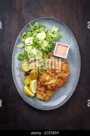 Gebratenes Wiener Schnitzel aus Kalbtopside mit Bratkartoffeln und Kopfsalat als Top-Ansicht auf einem modernen Design-Teller mit Kopie Platz Stockfoto