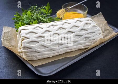 Rohes Kasseler Schweinesteak als Stück in Blätterteig und Eigelb als Nahaufnahme auf einer Grillplatte mit Kräutern angeboten Auf einem schwarzen Brett Stockfoto
