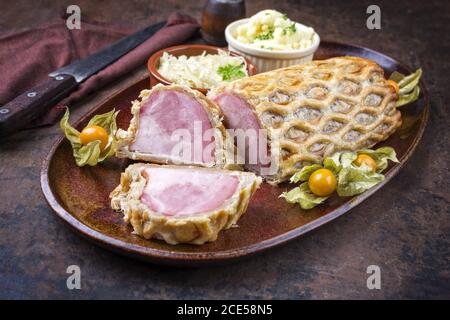 Hinterer Kasseler-Sattel von Schweinesteak mit Sauerkraut und Kartoffeln Salat als Nahaufnahme auf einem Teller mit Physalis angeboten Stockfoto