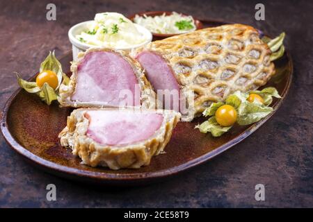 Hinterer Kasseler-Sattel von Schweinesteak mit Sauerkraut und Kartoffeln Salat als Nahaufnahme auf einem Teller mit Physalis angeboten Stockfoto