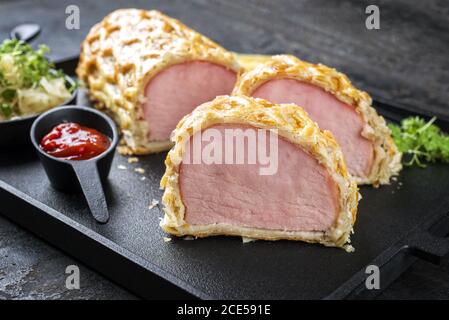 Kasseler Schweinesteak mit Sauerkraut und Ketchup als Nahaufnahme Angeboten auf einem modernen Design Gusseisen Tablett auf Holz Platine mit Stockfoto