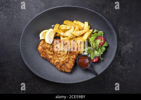 Frittierte Wiener Schnitzel aus Kalbsoberseite mit Pommes frites Und Salat als Draufsicht auf einem modernen Design-Teller Stockfoto