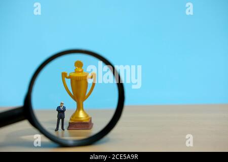 Miniatur Business-Konzept - Geschäftsmann vor golden stehen Trophäe und Lupe Glas Stockfoto