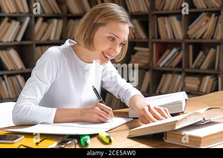 Glückliche junge Frau studiert in einer Bibliothek. Stockfoto