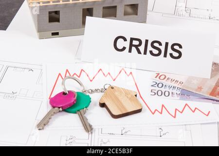 Schlüssel mit Hausform, Währungen Euro, Abwärtsgraphen und Inschrift Krise auf elektrischen Baudiagramme des Hauses. Immobilienkrise Stockfoto