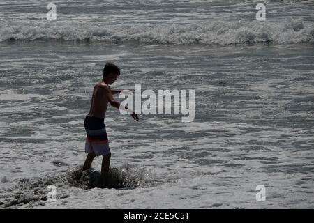 Eine Silhouette eines Jungen Skim Boarding in der Nähe der Ozeane Rand am Strand. Stockfoto