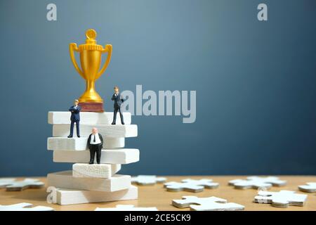 Miniatur Business-Konzept - Geschäftsmann auf weißen Treppe Leiter stehen Mit goldener Trophäe darüber Stockfoto