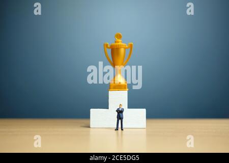 Miniatur-Geschäftskonzept - Geschäftsmann vor Weiß stehen Siegerpodium mit goldener Trophäe Stockfoto