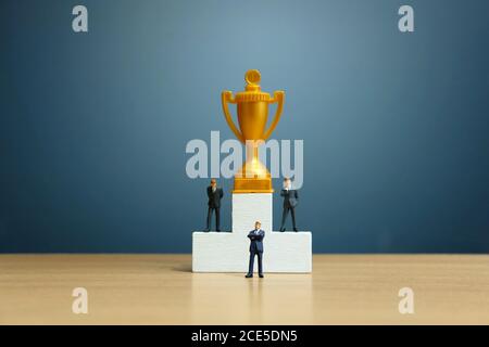 Miniatur-Geschäftskonzept - Geschäftsmann vor Weiß stehen Siegerpodium mit goldener Trophäe Stockfoto