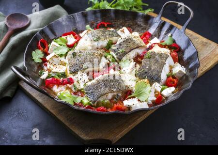 Traditioneller gebratener griechischer Kabeljau-Fischfilet-Auflauf mit Feta-Käse Und Gemüse als Nahaufnahme in einer rustikalen schmiedeeisernen Pfanne Stockfoto