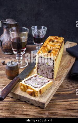 Traditionelle französische Pate en Croute mit Gänsefleisch und Leber Als Nahaufnahme mit Rotwein auf einem Holzbrett Stockfoto