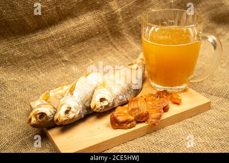 Getrockneter Fisch, getrockneter Kaviar und ein Bierkrug auf einem hölzernen Servierbrett. Nahaufnahme Stockfoto