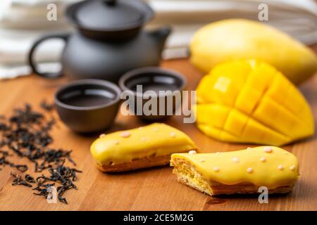 Eclair ein französisches Sahneteig mit Mango-Geschmack Die Hälfte zeigt das Innere des Fruchtbläschens und den Nachmittag Teeset Stockfoto