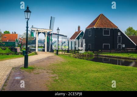 Fesselnde holländische Landstraße mit traditioneller Holzwindmühle und grasenden Schafen im Garten, Zaanse Schans touristisches Dorf, Niederlande, Stockfoto