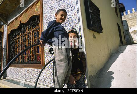 14.11.2010, Fes, Marokko, Afrika - zwei junge Racker spielen auf der Straße vor einem Haus, während einer von ihnen seine Zunge ausstreckt. Stockfoto