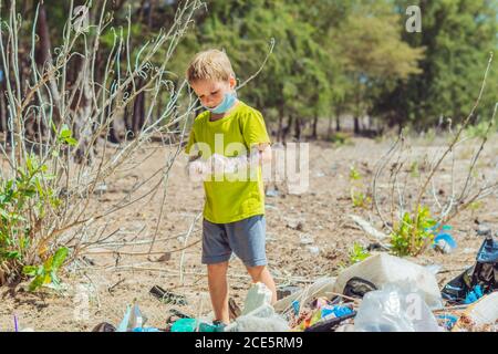 Volunteer Junge in Gesichtsmaske hilft, Müll, der Strand in der Nähe von Wald verschmutzen abholen. Problem der verschütteten Müll Müll Müll Planeten Verschmutzung Umwelt Stockfoto