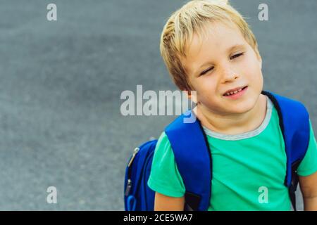 Lustig schelmisch niedlich blonde Junge mit Sommersprossen blauen Rucksack aus der Schule oder Kindergarten, künstlerische Emotionen Gesichtsausdruck. Micro Moments einfach Stockfoto