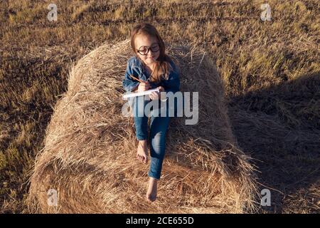 Luftaufnahme. Ein Mädchen sitzt auf einem Heuhaufen und malt eine Landschaft. Blick von oben. Ausgewählter Fokus Stockfoto