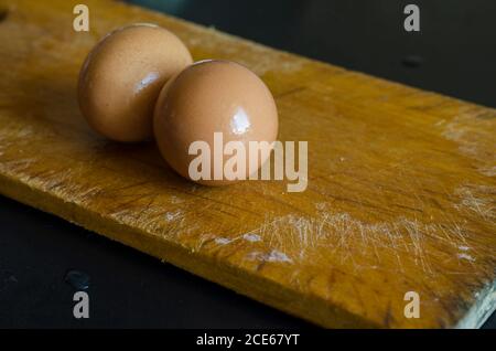 Zwei braun gekochte Hühnereier auf dem Schneidebrett. Nahaufnahme von feuchten Hühnereiern in Muscheln. Kochen. Selektiver Fokus. Stockfoto