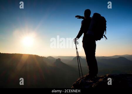 Scharfe Silhouette eines großen Mannes auf der Spitze des Berges mit Sonne im Rahmen. Reiseführer in den Bergen Stockfoto