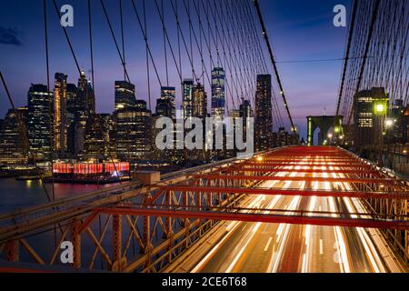 Wolkenkratzer in Lower Manhattan bei Dusk und Brooklyn Bridge mit leichten Pfaden. Abend in New York City, NY, USA