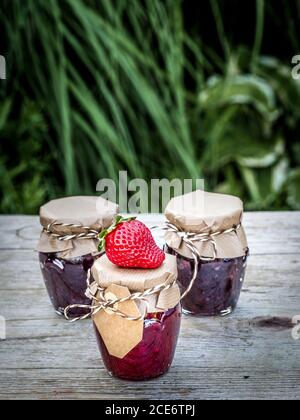 Drei Gläser hausgemachte Marmelade aus Erdbeeren und Himbeeren auf Vintage-Holztisch im Garten. Nahaufnahme mit Kopierbereich. Stockfoto