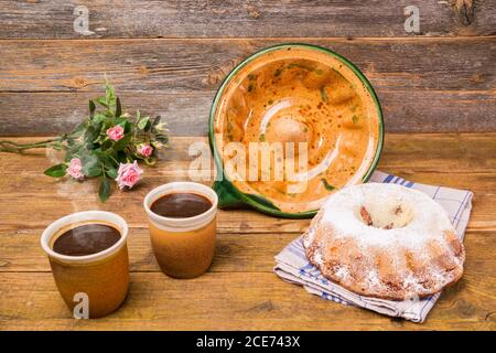 Ein Gugelhupf mit seiner Keramik-Backform und zwei Tassen Kaffee und ein Feld Blumen Geburtstagsstrauß auf einem Holztisch mit einem hölzernen Hintergrund. Und ein Stockfoto